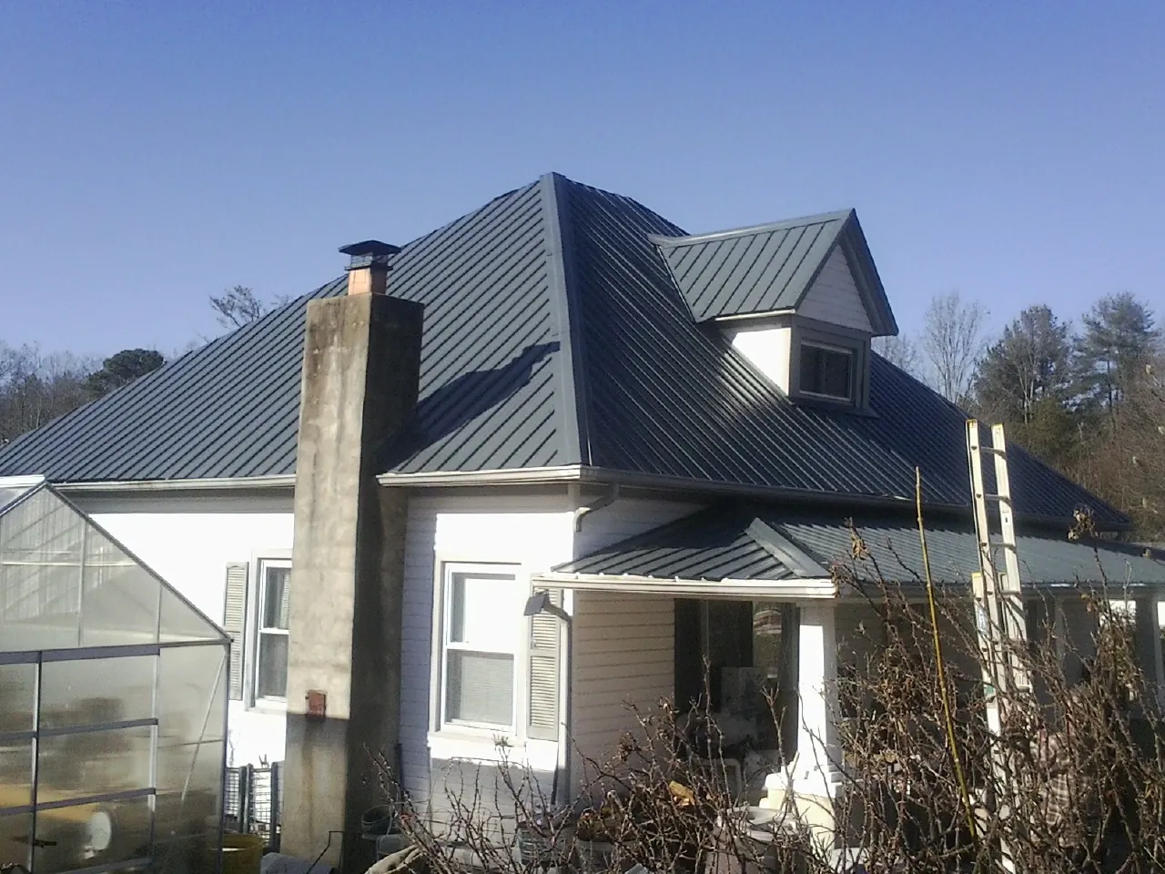 Dark blue standing seam metal roof on a white farmhouse with dormer — Slate & Tile Roof Repair by Roofing Brothers in Mc Intosh