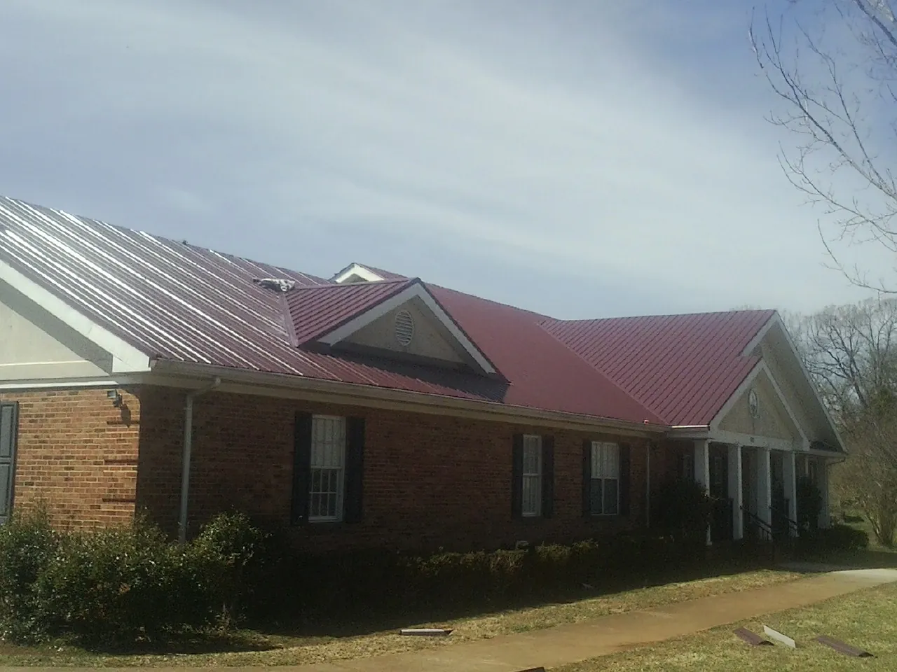 Red metal roof with gabled entries on a long brick building, from a Hail Damage Roof Repair job in Mc Intosh