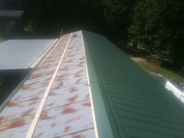 Old rusted panels beside newly installed green metal roofing — Wind Damage Roof Repair by Roofing Brothers in Mc Intosh