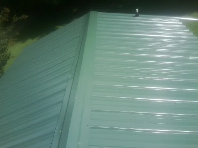 New green metal panels meeting at the ridge of a roof — Flat Roof Repair work by our crew in Mc Intosh