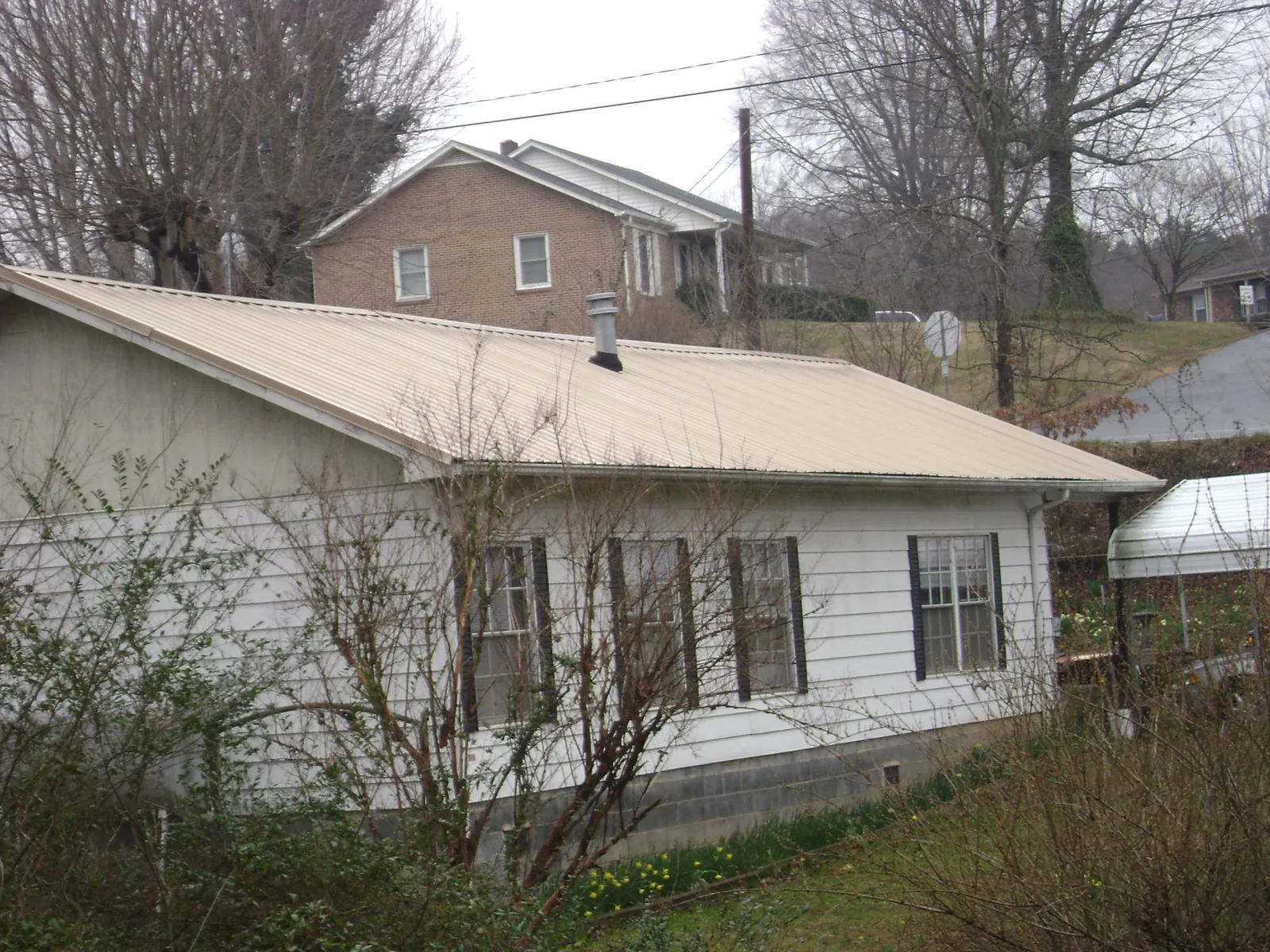 Tan metal roof on a white sided house set into a hillside — Commercial Roofing by Roofing Brothers in Mc Intosh
