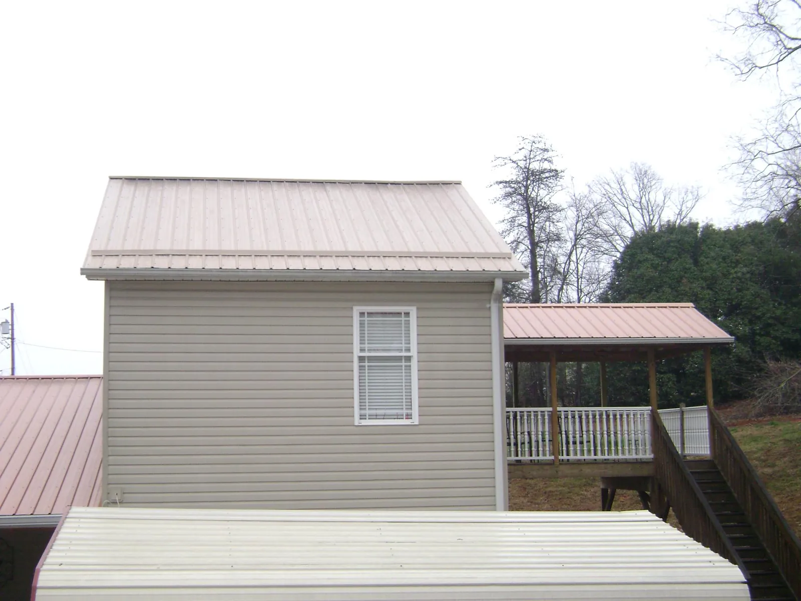 Tan metal roofs on a two story addition and attached porch, from a Roof Replacement job in Mc Intosh